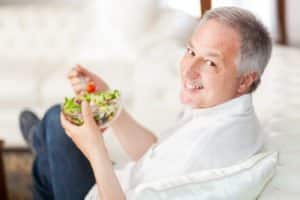 Mature man eating a healthy salad sitting on his couch